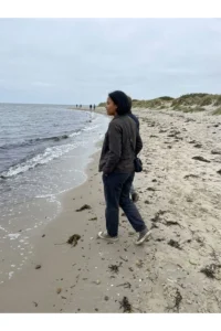 An adult looking out over a breezy sandy beach shoreline.