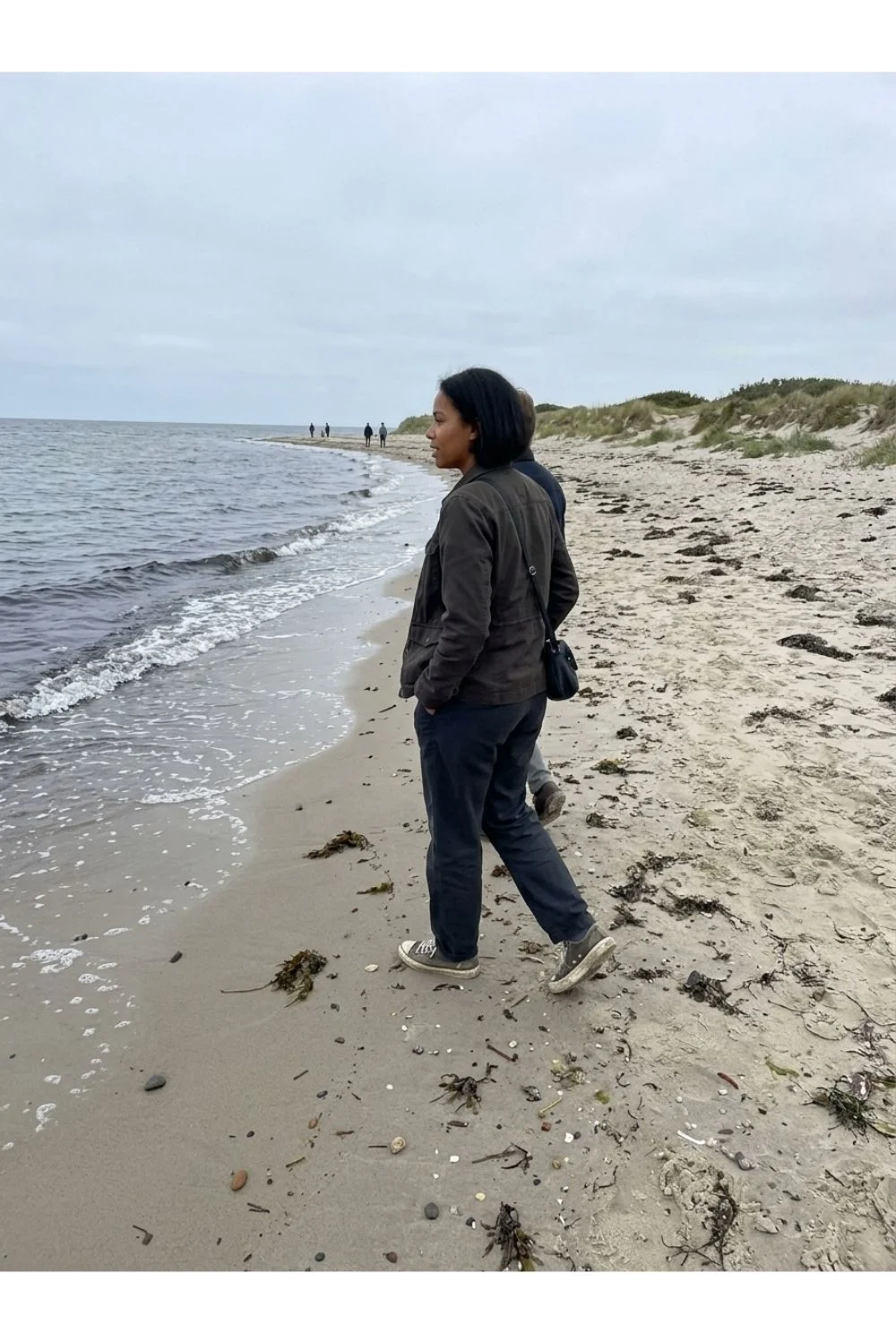 An adult looking out over a breezy sandy beach shoreline.