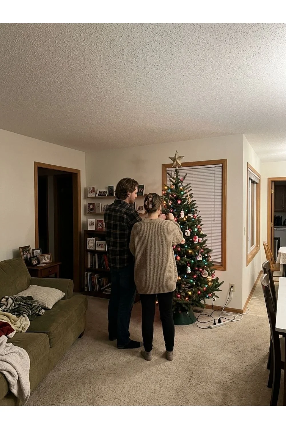 Two adults standing near a modest Christmas tree inside a home.