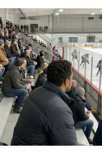 Spectators seated in a small community ice hockey rink.
