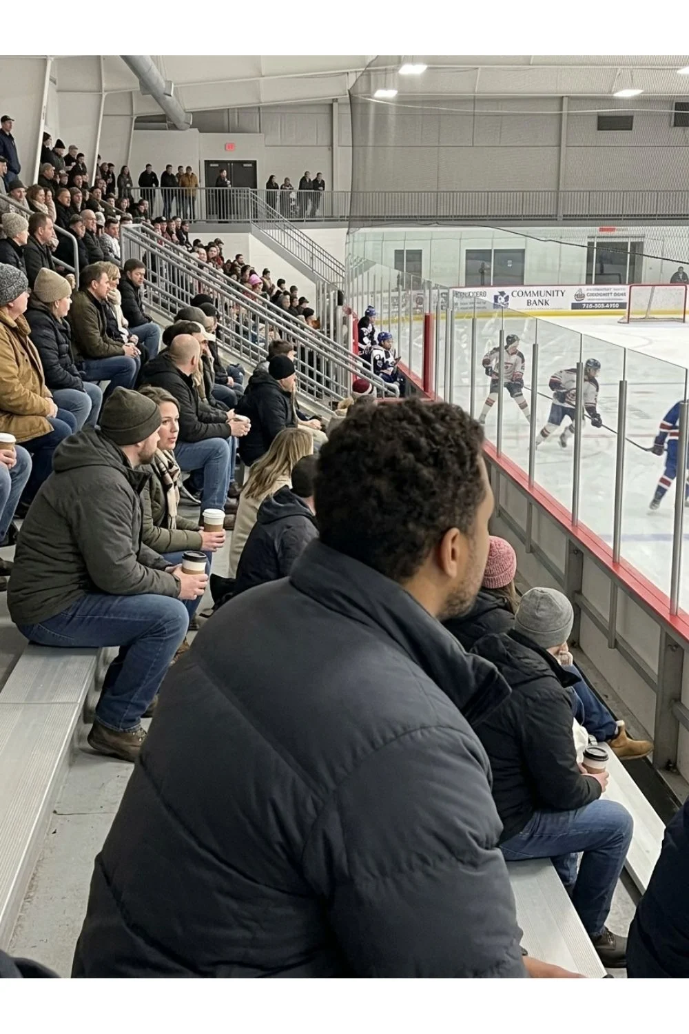 Spectators seated in a small community ice hockey rink.