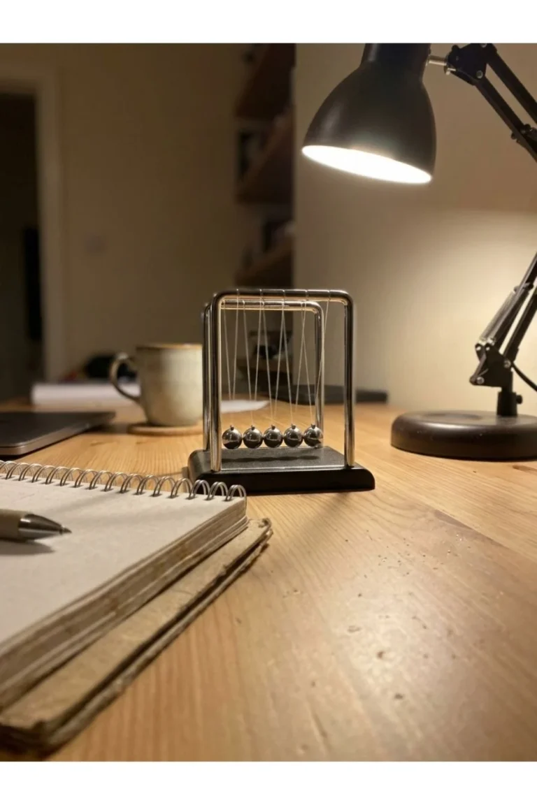 A small Newton cradle on a desk under a task lamp.