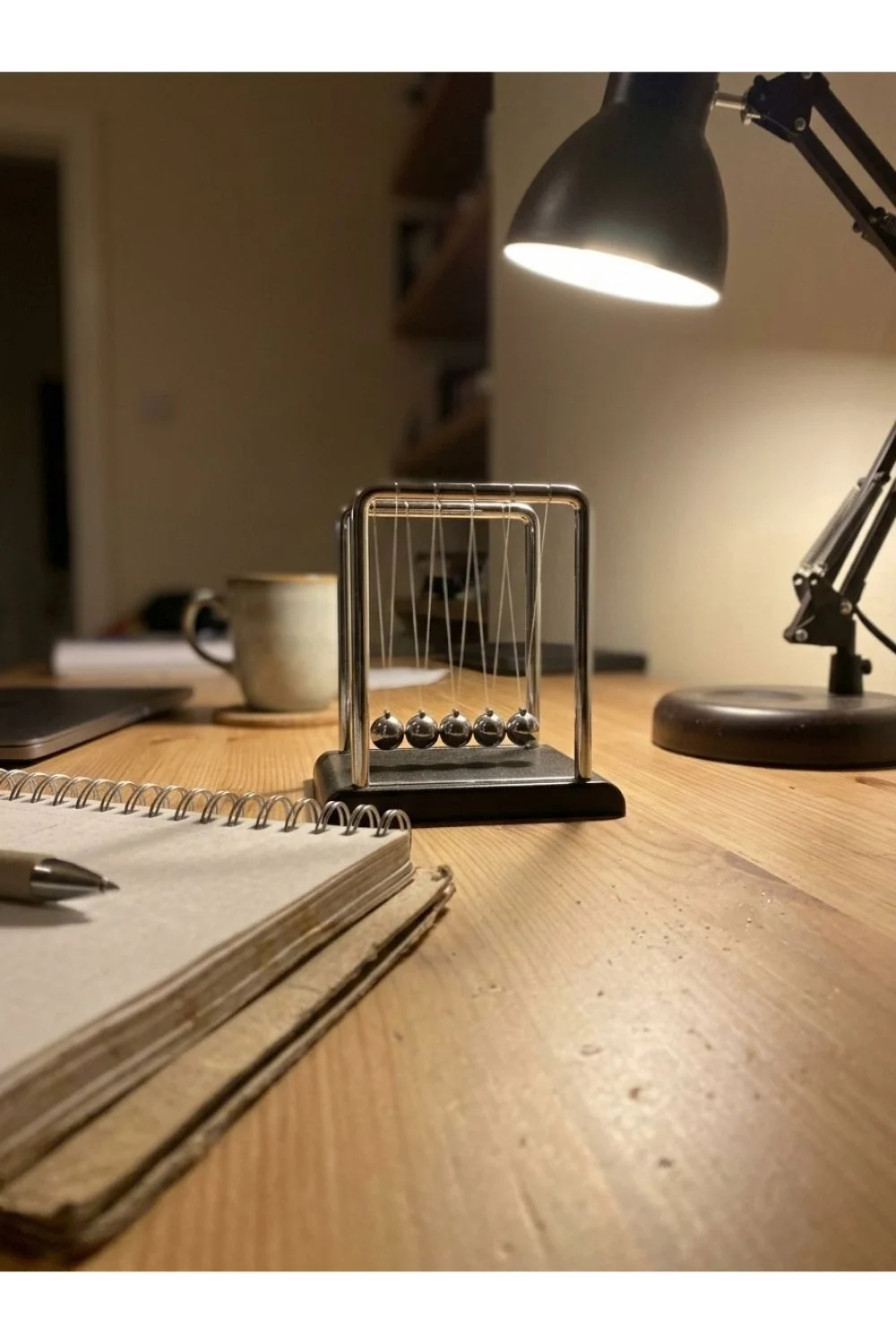 A small Newton cradle on a desk under a task lamp.