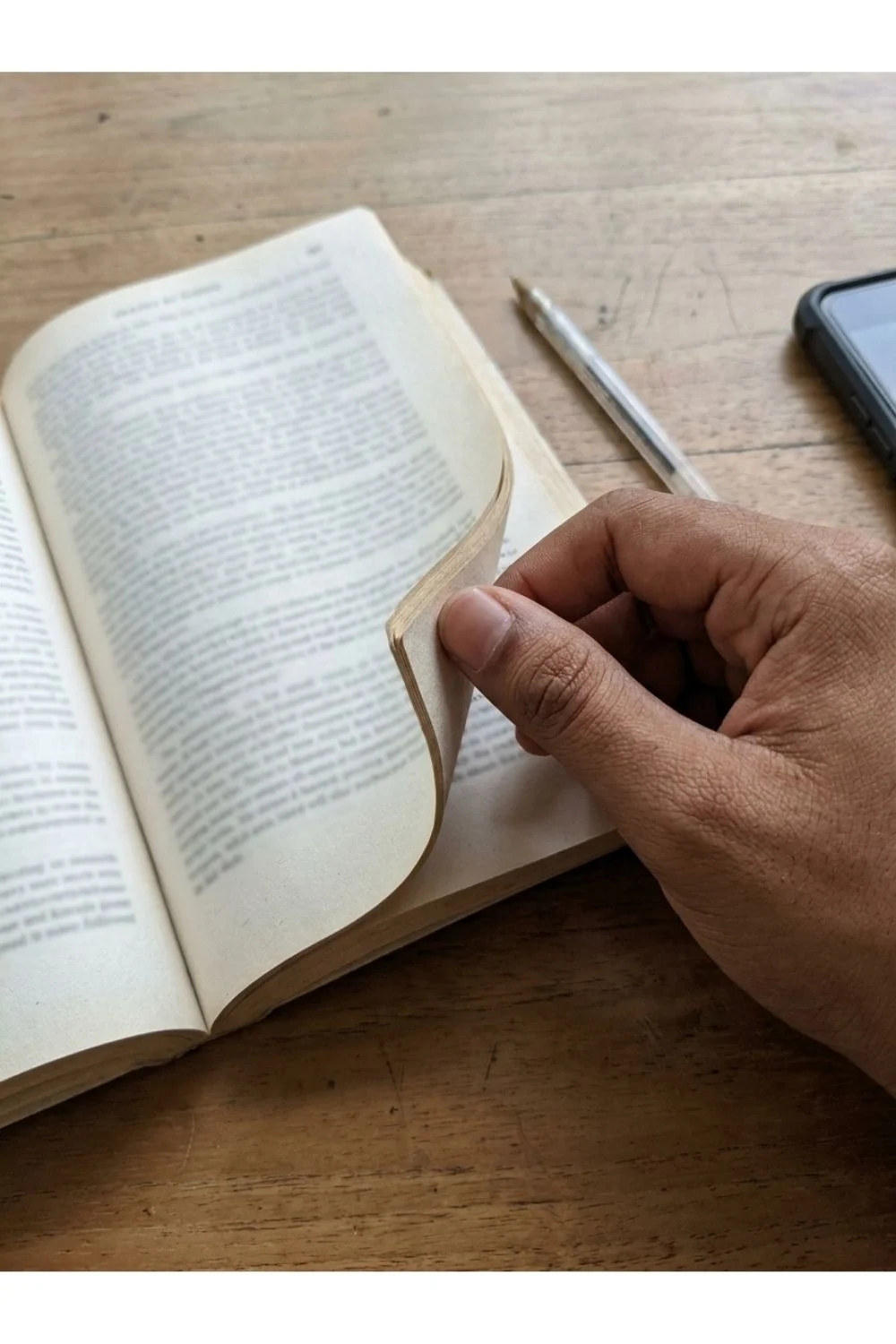 A hand turning a page in an open paperback book.