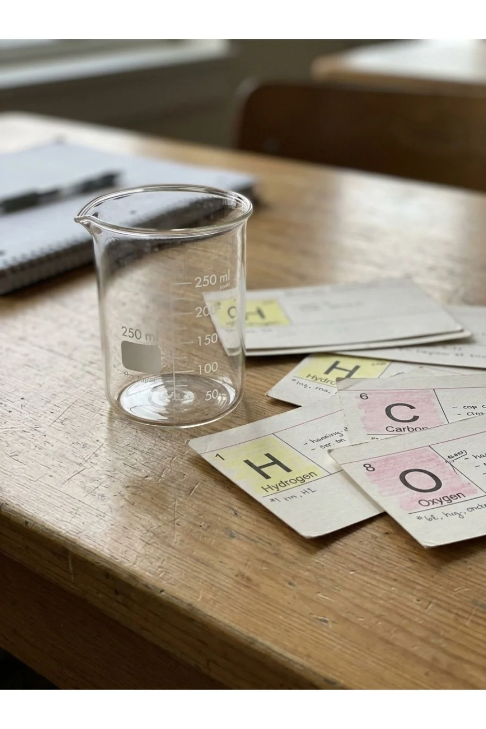 An empty beaker and loose element cards on a science classroom desk.