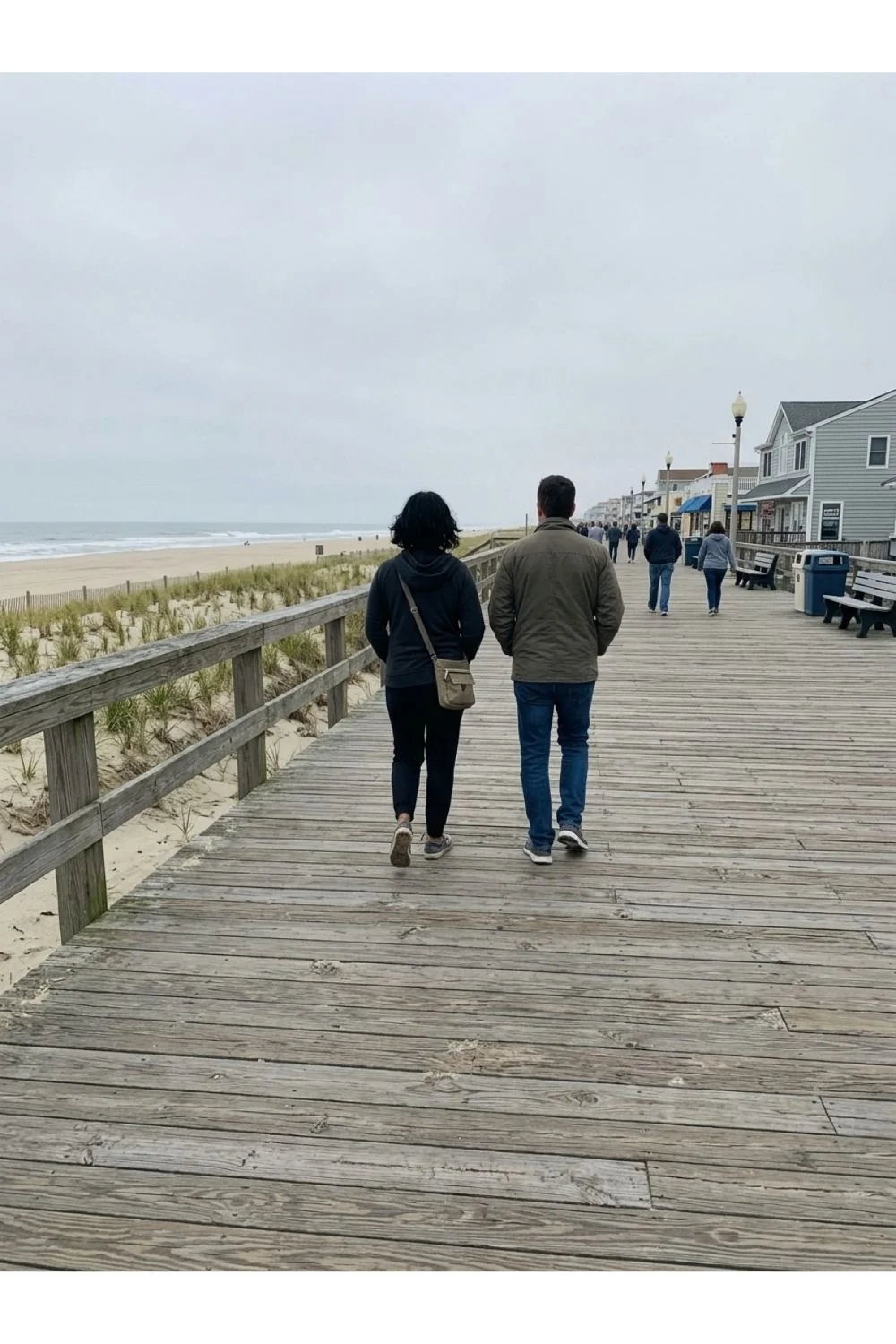 Two adults walking along a wooden boardwalk by the beach.