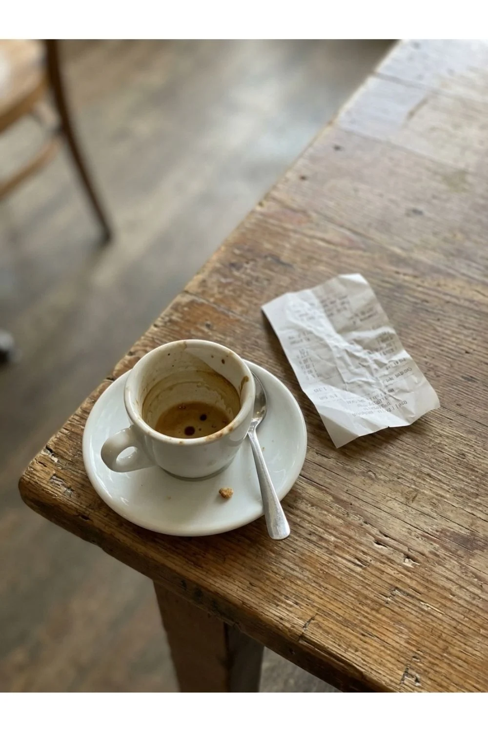 An almost empty espresso cup with a spoon on a wooden café table.