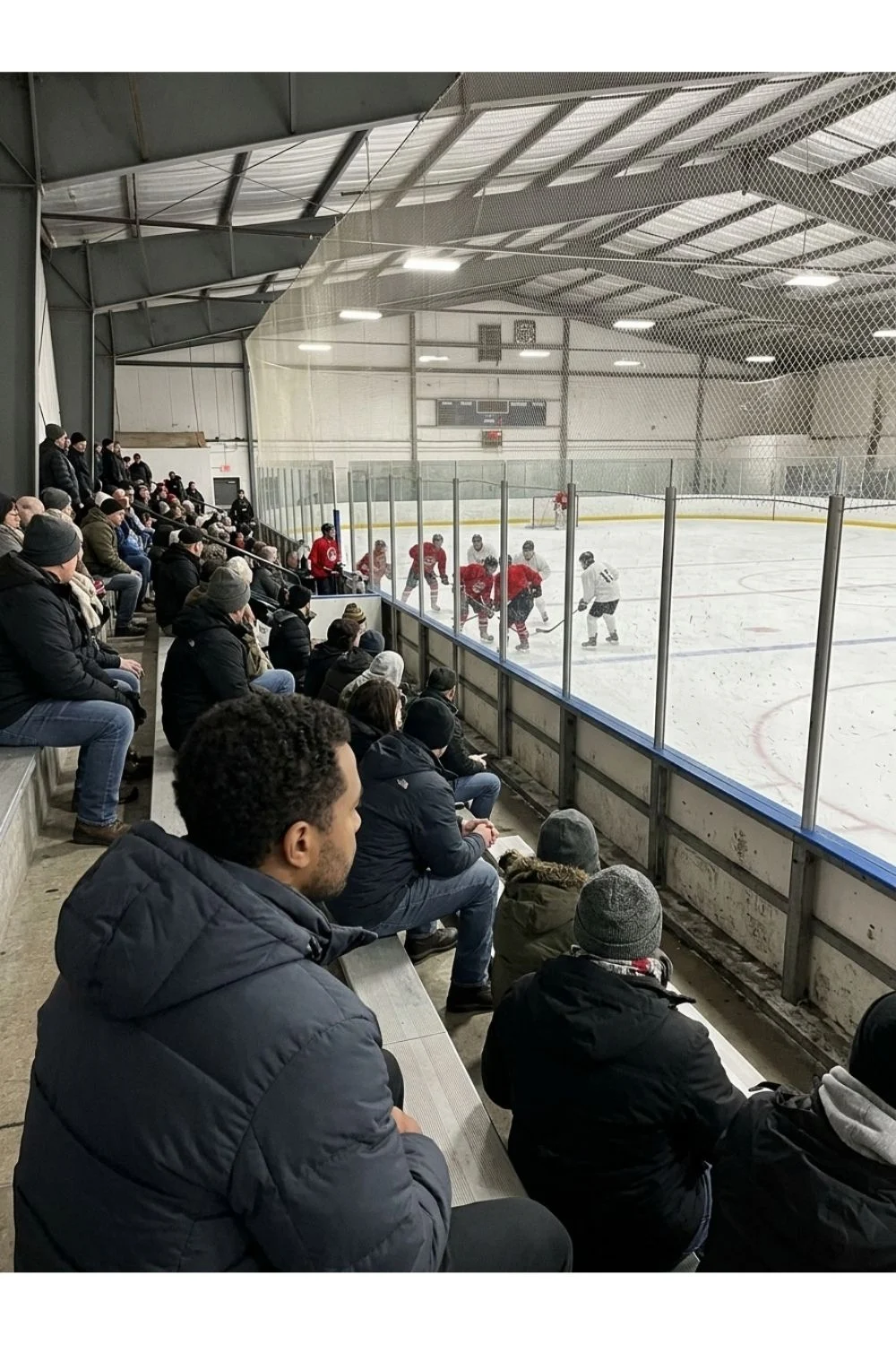 Spectators looking toward an indoor community ice hockey rink.