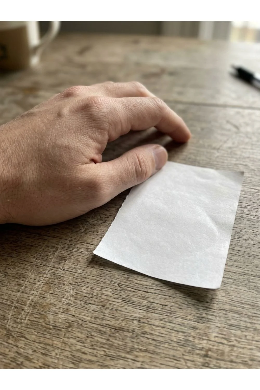 A hand resting beside a blank paper note on a wood tabletop.