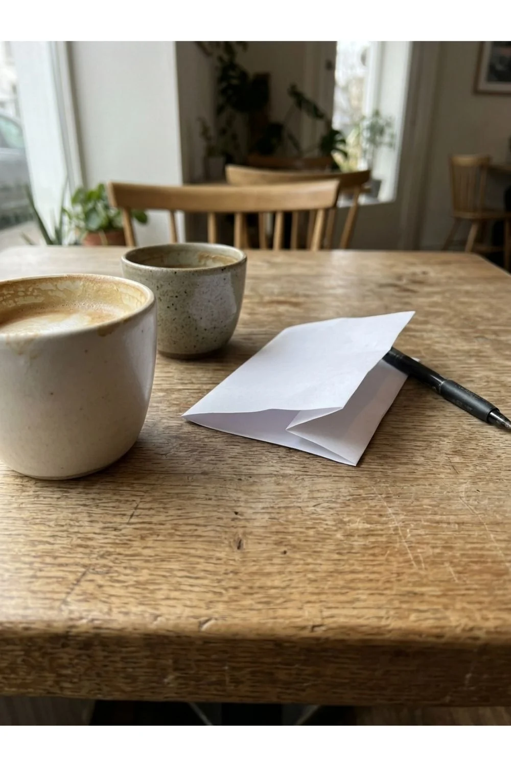 Two mugs and a folded blank card on a wooden table.