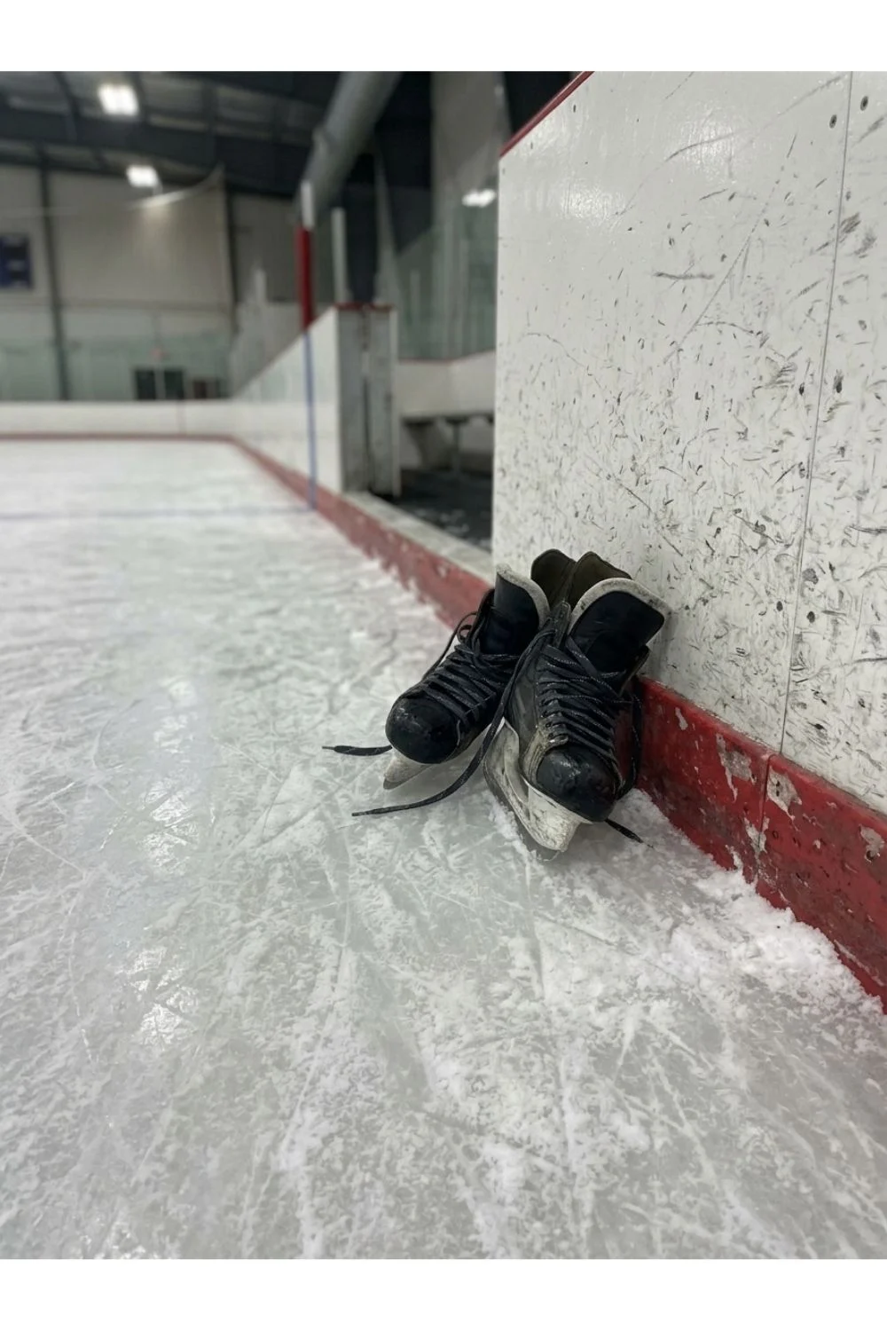 A pair of worn skates resting beside the boards of an ice rink.